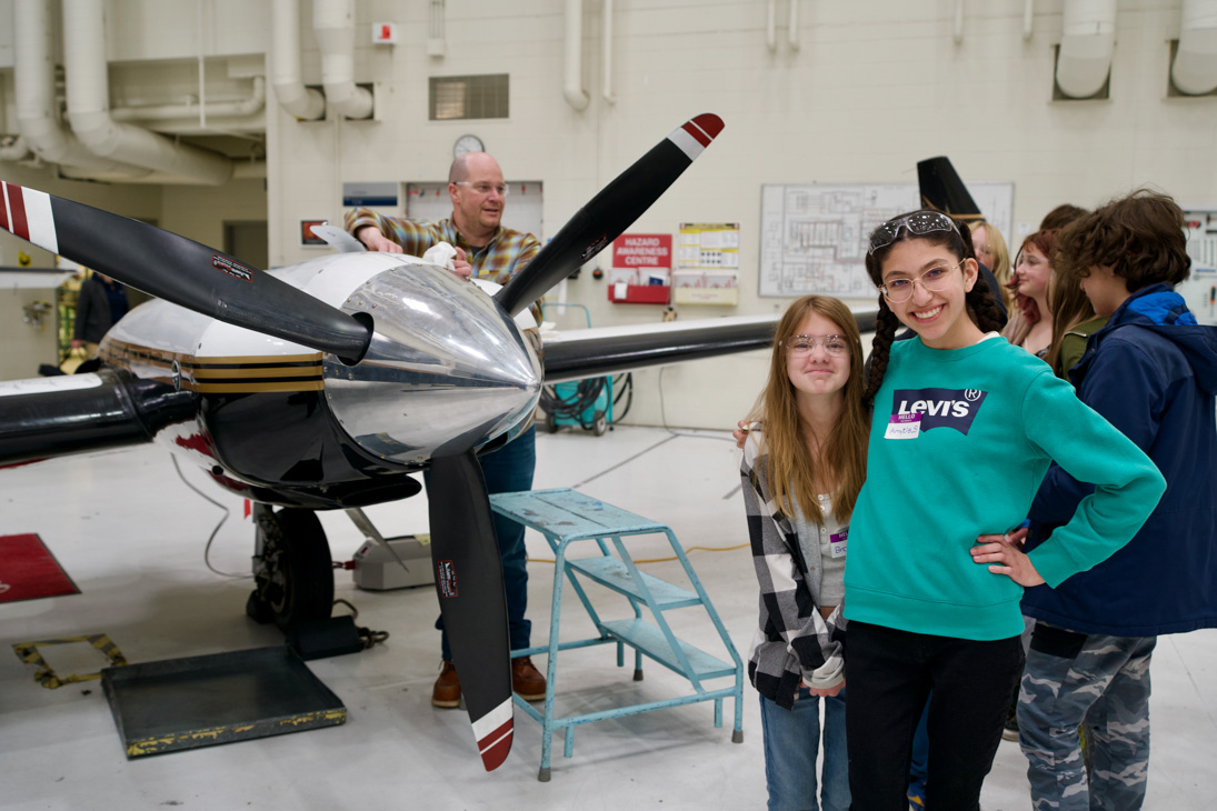 Students stand smiling in front of a prop plane.