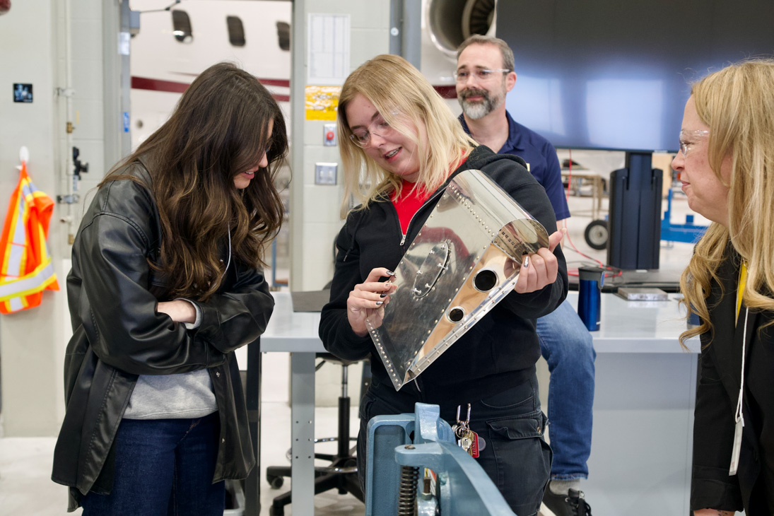 An instructor shows a junior high student rivets in sheet metal.