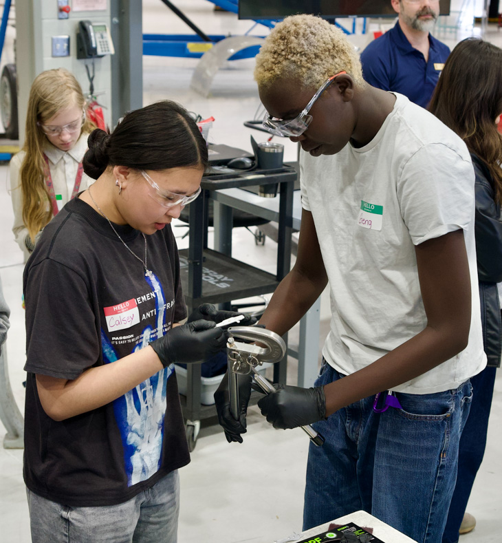 An instructor helps a student work on riveting sheet metal.
