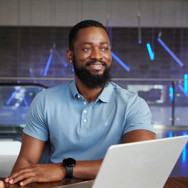 A man at SAIT smiles in front of an open laptop and looks off in the distance.