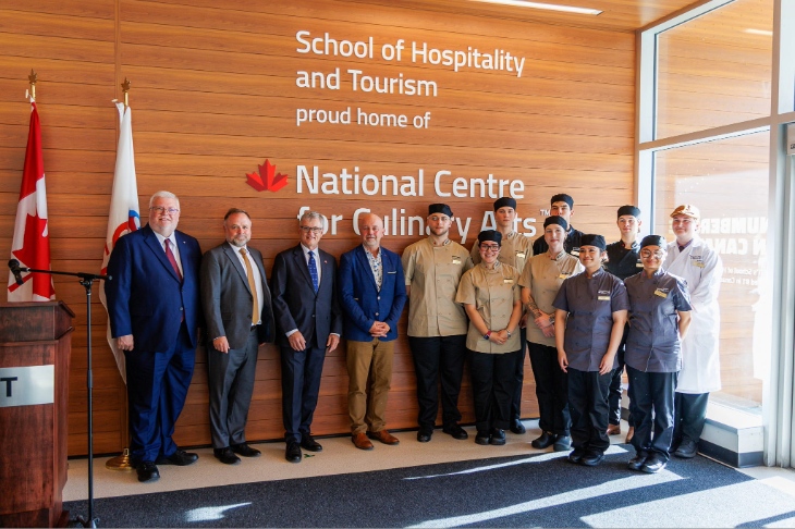 A group of people stand in front of a sign that reads "School of Hospitality and Tourism home to the National Centre for Culinary Arts"