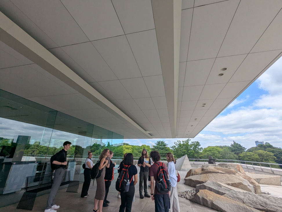 Group of people gathered beneath the large overhang of a modern building.
