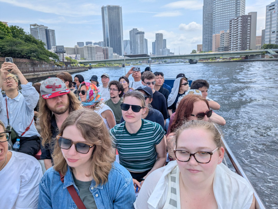 Group of people riding in an open boat with a city skyline across the water.