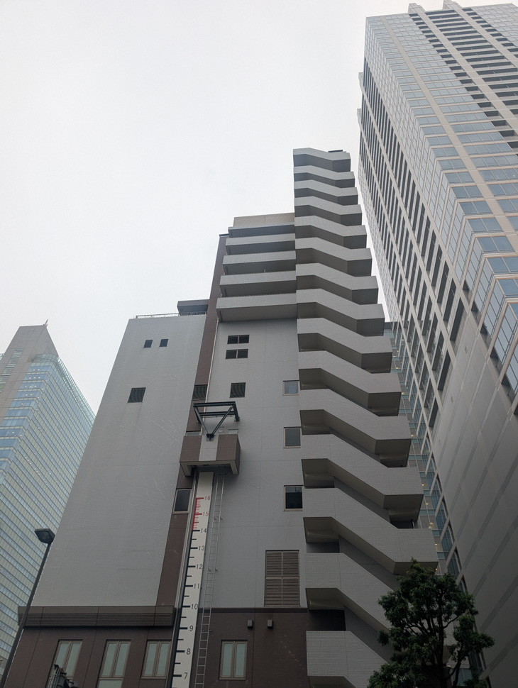 Low-angle view of a tall, narrow building surrounded by highrises.