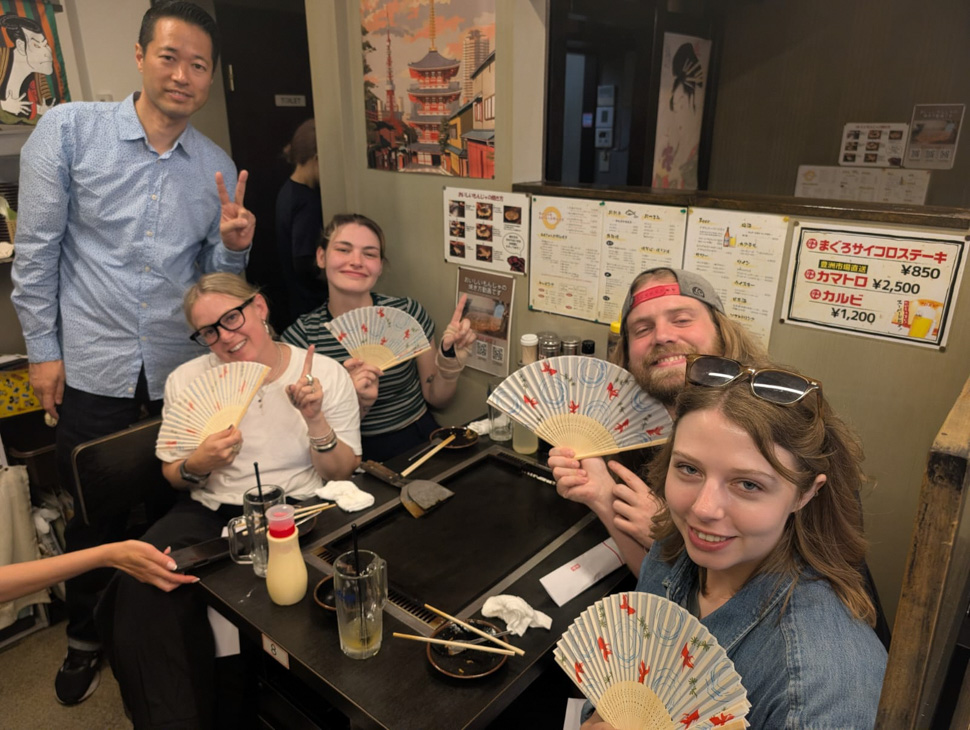 Group of people seated around a restaurant table holding decorative fans.