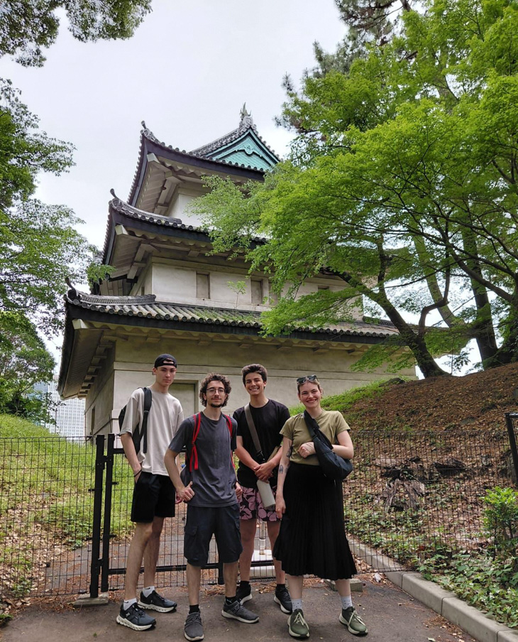 Group of people standing in front of a traditional Japanese castle surrounded by trees.