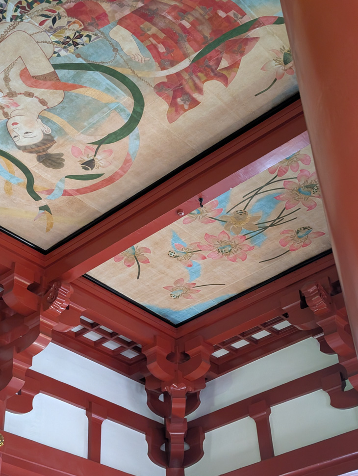 Ornately painted ceiling and red wooden beams of a traditional Japanese building.