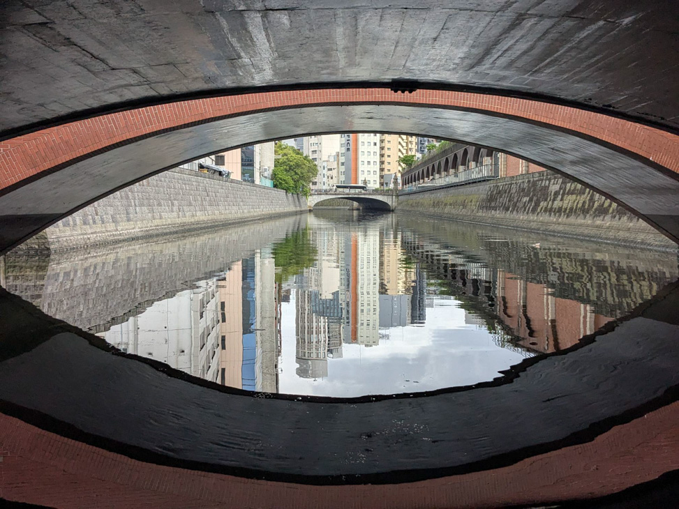 Buildings reflected in the water beneath an arched bridge.