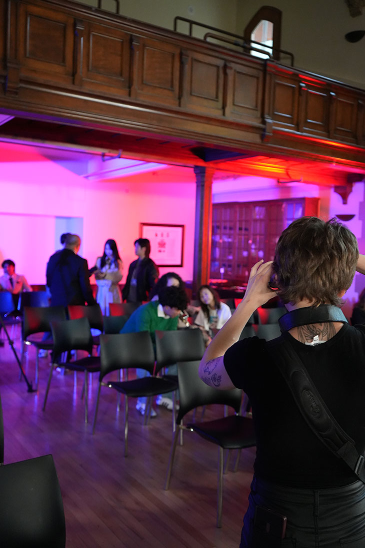 student behind the camera photographing a group of people against a pink and blue backdrop at the FutureTech event in February 2026