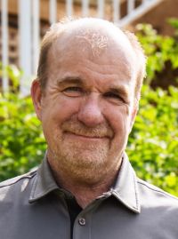 Professional headshot of Graeme Zander smiling with outdoor greenery backdrop.