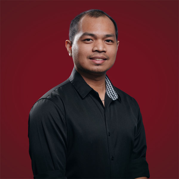 Francisco Pilapil in a black shirt with a checkered collar, set against a solid red background.