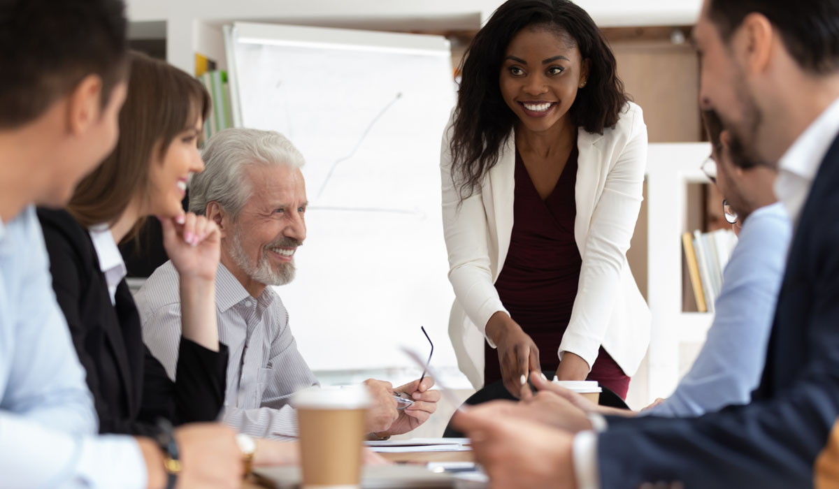 A diverse group of professionals engaged in a collaborative meeting, with a smiling woman presenting ideas to her colleagues.
