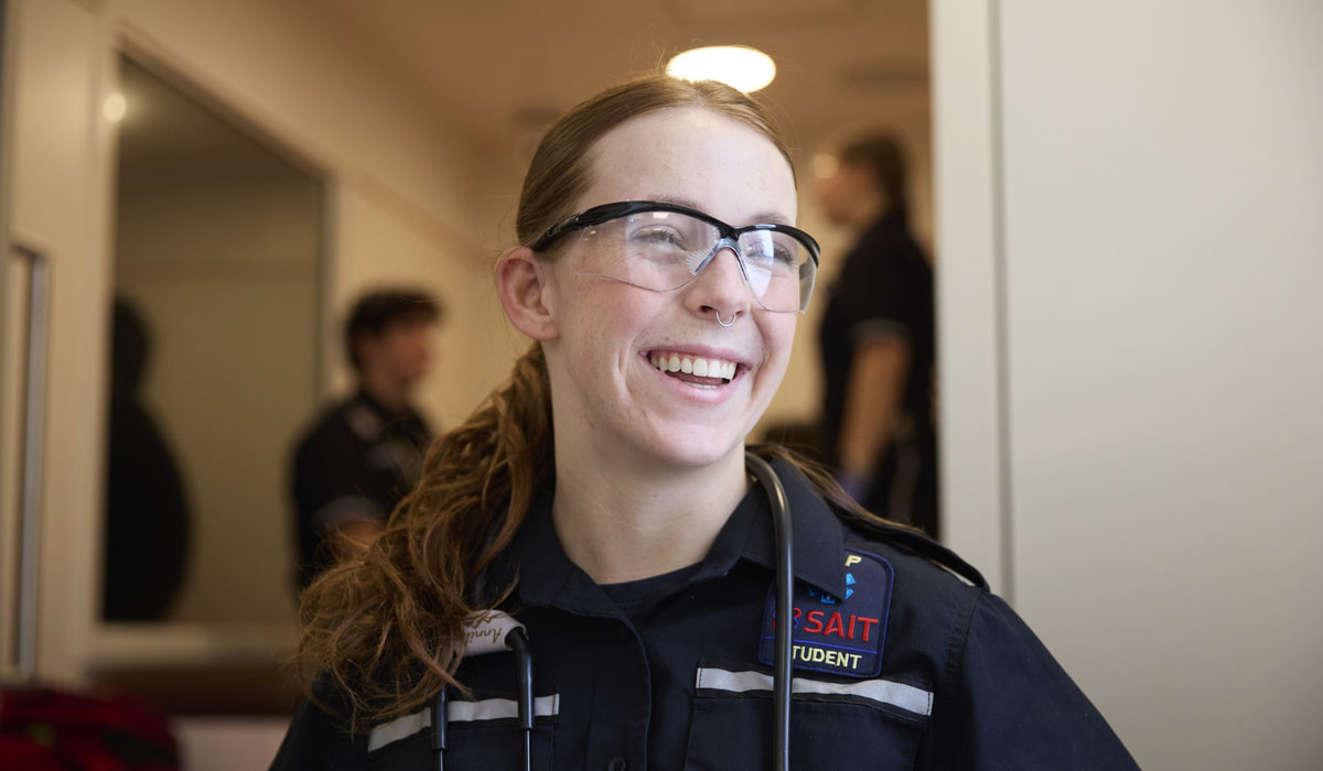 A smiling EMT student in uniform with a stethoscope.