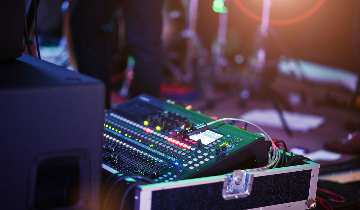 A digital audio mixer with colorful LED lights, used for sound mixing at a live music event.