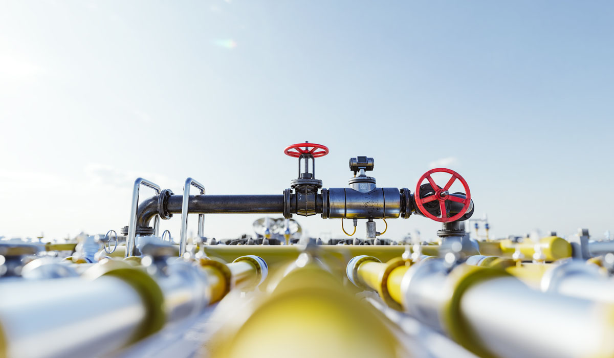 Industrial pipeline featuring control valves and bright red handle indicators against a clear blue sky.
