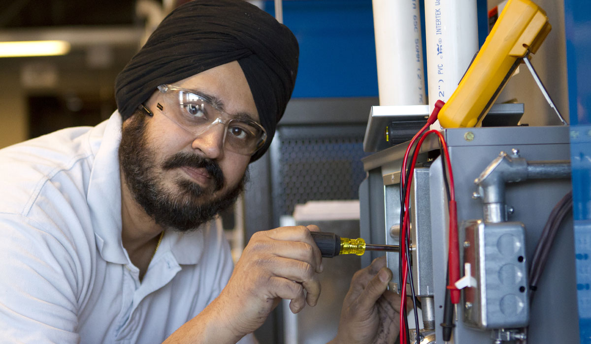 A technician wearing safety glasses works on electrical equipment with a screwdriver.