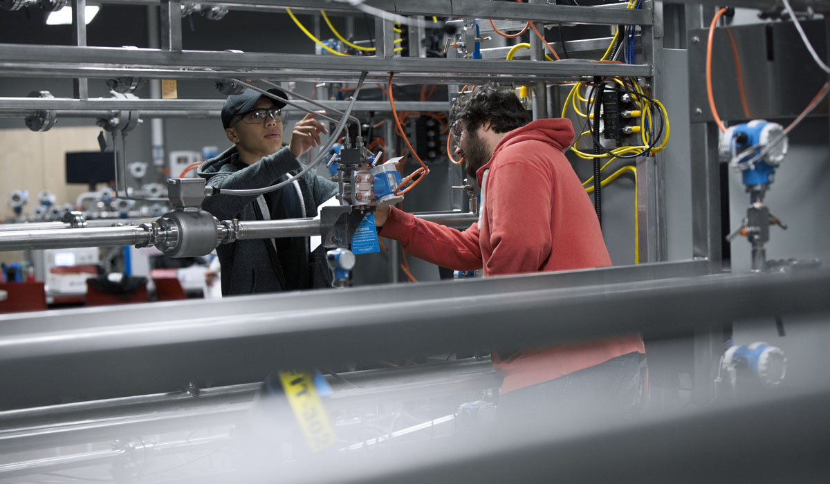 Two individuals collaborating on a mechanical setup, working with pipes and instruments.