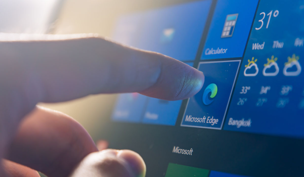 A close-up of a finger tapping the Microsoft Edge icon on a Windows interface.