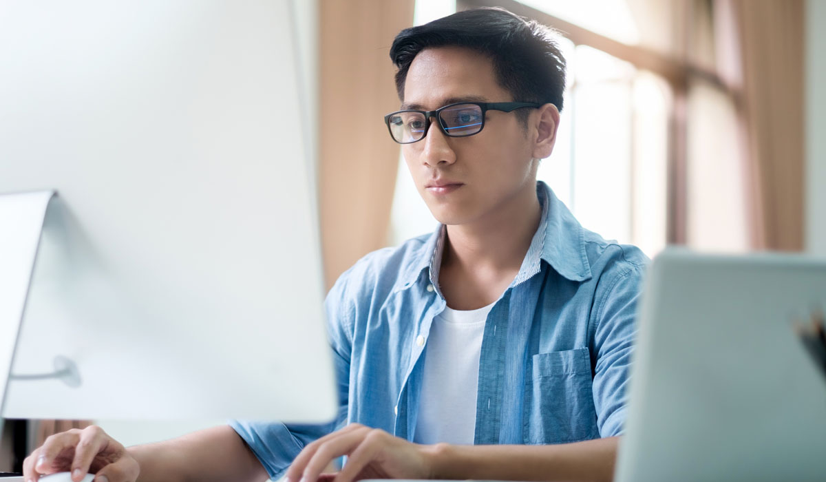 A focused young man wearing glasses works at a computer desk, emphasizing concentration and productivity.