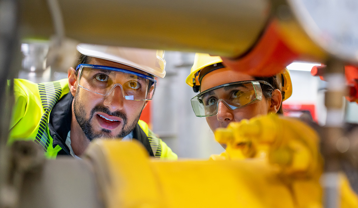 Two men wearing hard hats investigating pipes.