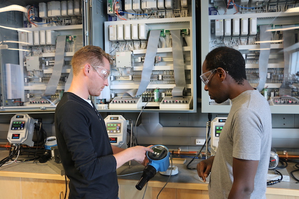 Two men wearing safety glasses look at a Programmable Logic Controller (PLC) in a SAIT electrical lab.