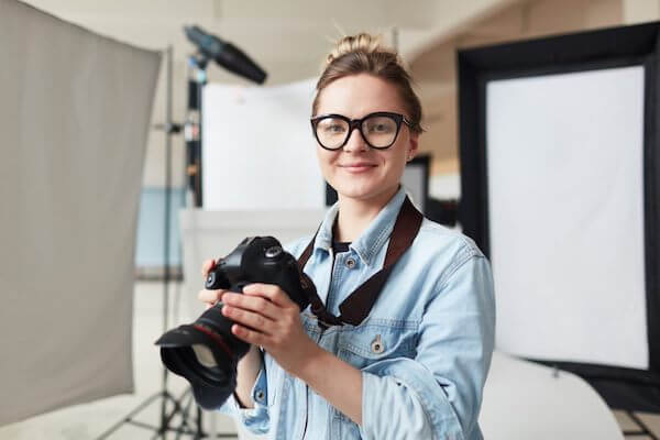 A woman smiles while holding a camera in a studio. 