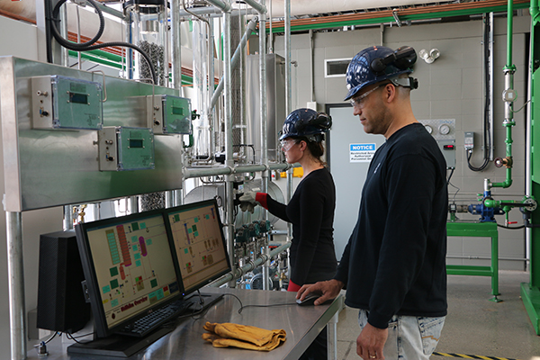 A man and a woman working in a lab while wearing hard hats