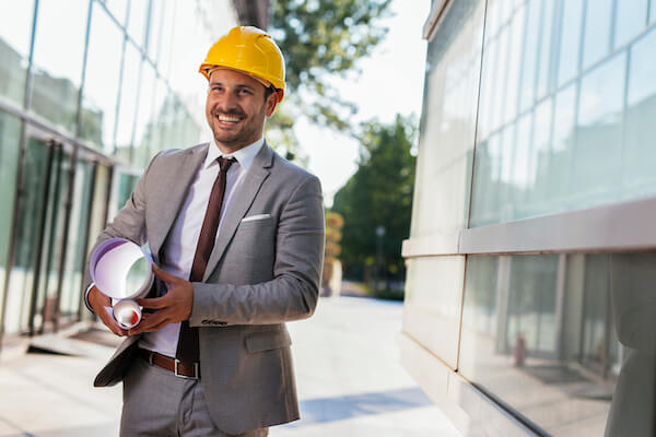 A person wearing a hard hat walking with drawings
