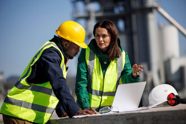 Two people wearing sefty vests looking over plans and talking
