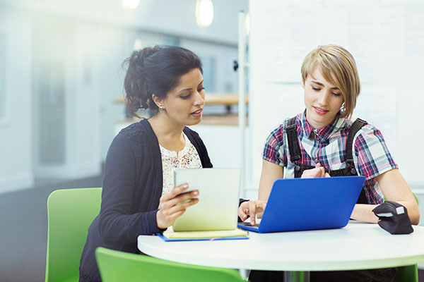 A financial services advisor speaks with a client at a desk. They look at a small laptop together.