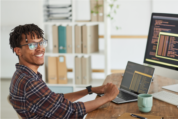 A man with his laptop on a desk smiling towards the camera