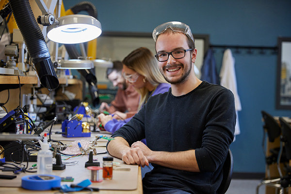 A young man wearing safety glasses rewires an electrical panel.