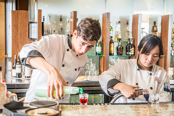 Two students pouring mixed drinks onto glasses