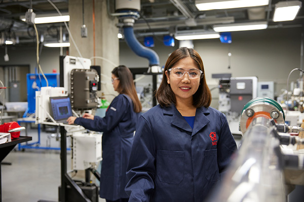 Student in the lab wearing ppe smiles at the camera
