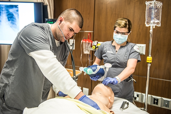 Two students wearing safety glasses and face masks monitor a Resusci-Anne doll's lung capacity after incubation. 