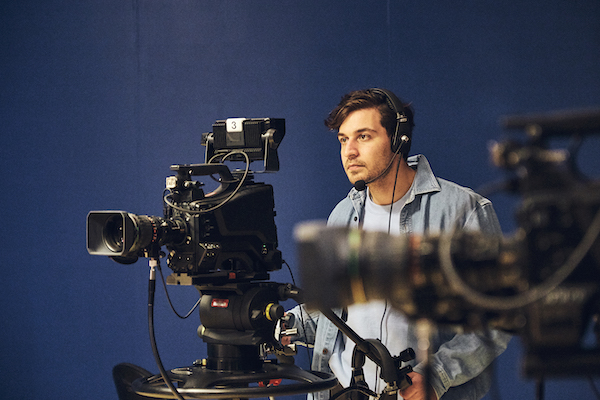 Man sits behind a tv camera.