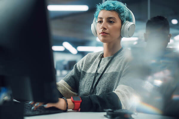 A women sits infront of two computer screens. She is looking back and smiling in front of larger routers.