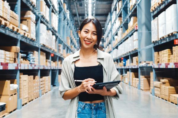 a woman smiling, holding a clipboard in a warehouse.