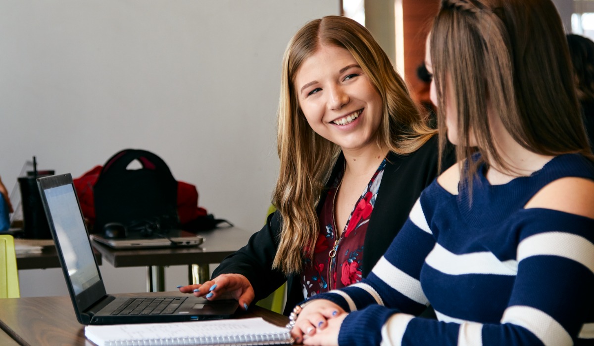 Two students engaged in a collaborative discussion while working on a laptop in a study setting.