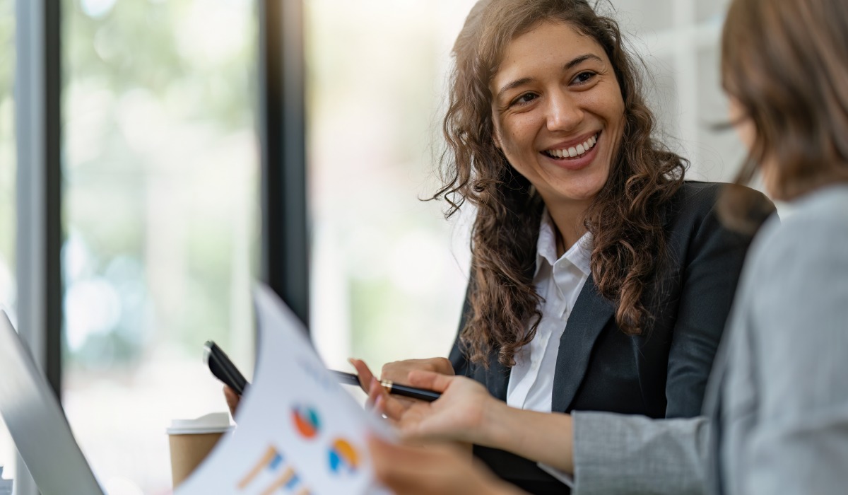 Two business professionals in a modern office setting engage in a friendly discussion while reviewing documents with charts.