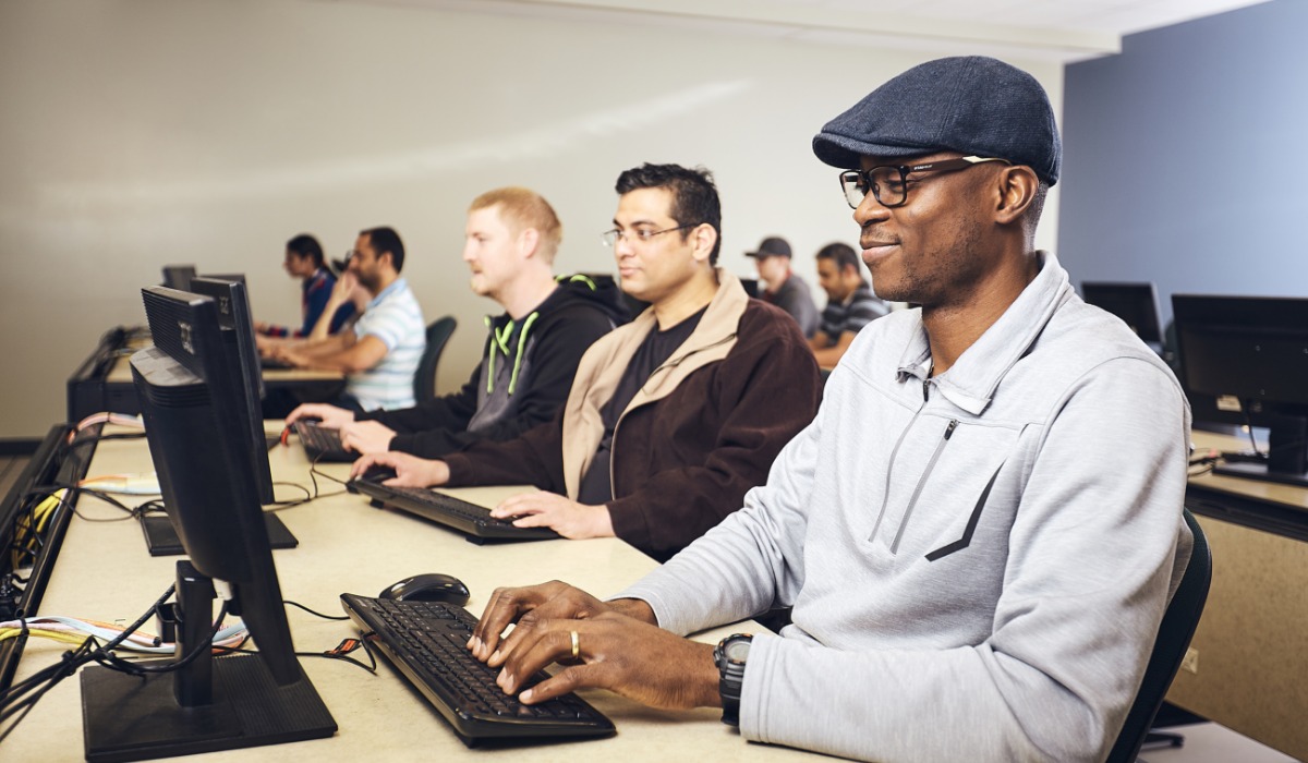 Group of diverse individuals focused on computers in a classroom setting.