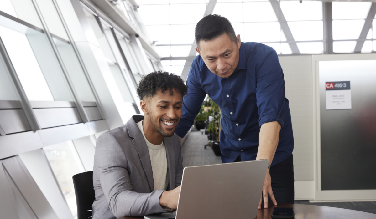 Two men collaborating at a laptop in a modern office setting, showcasing teamwork and productivity.