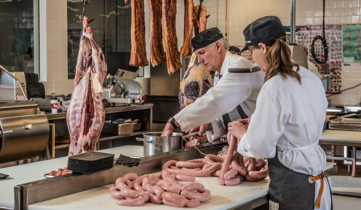 Butchers working collaboratively in a meat processing facility, preparing sausages and handling various cuts of meat.