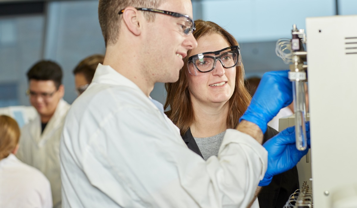 Students in lab coats and safety goggles collaborating on a scientific experiment in a laboratory setting.