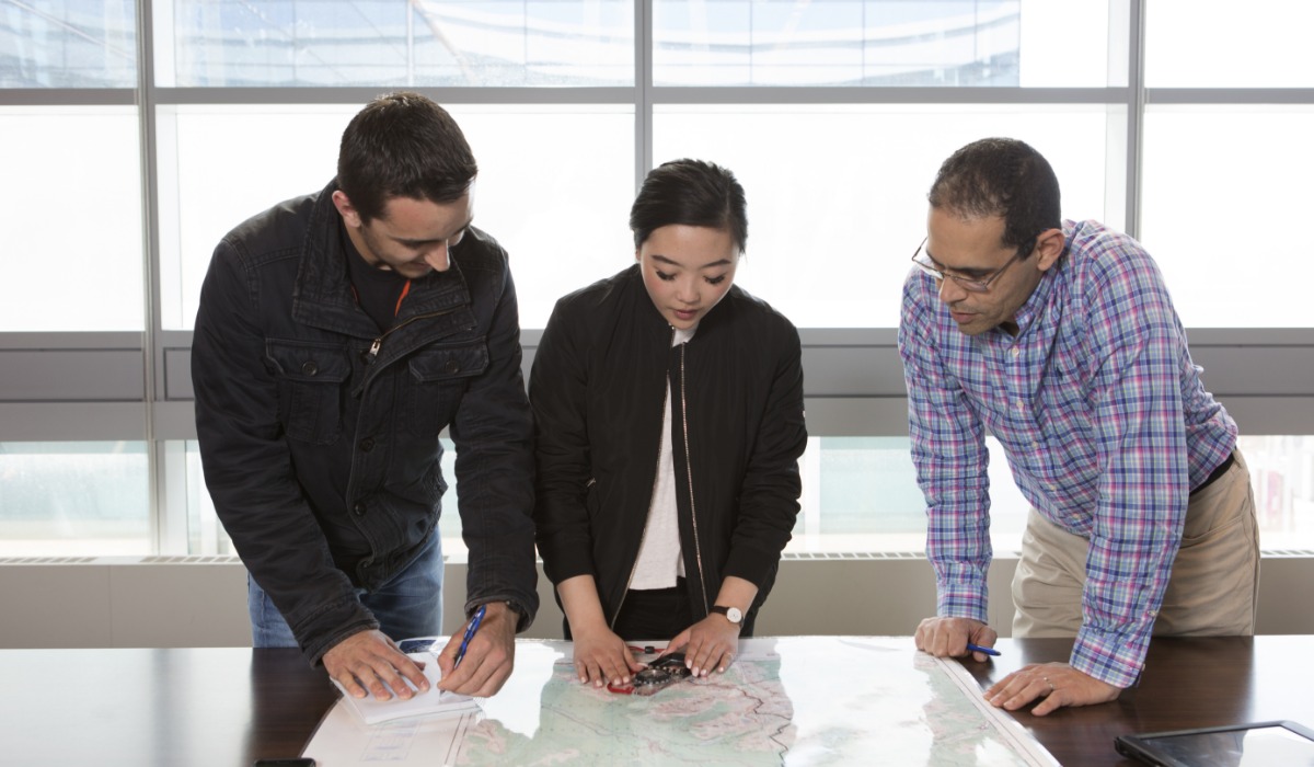 Three students collaboratively examining a large map on a table.