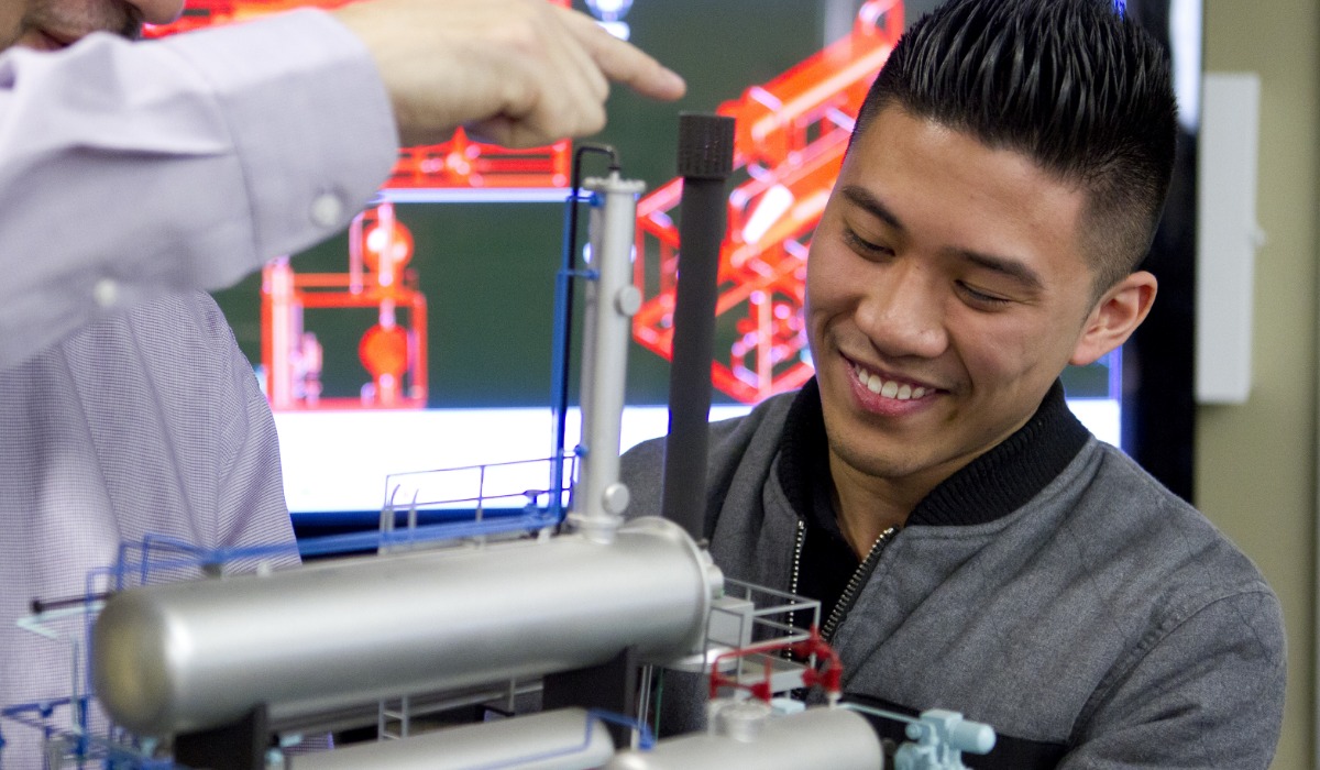 A student examines a technical model while engaged in a discussion with an instructor.