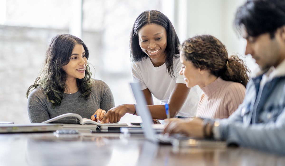 Group of diverse students collaborating and discussing over study materials in a light-filled study area.