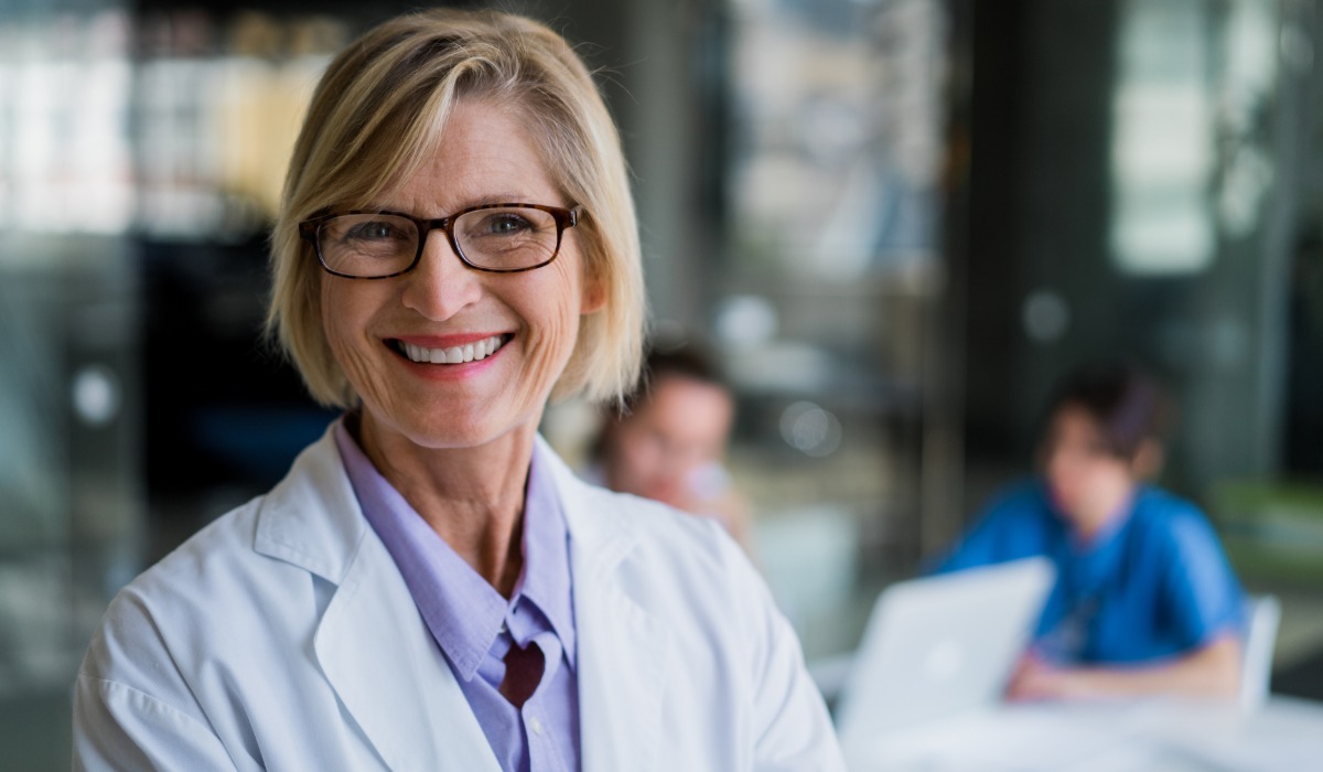 Smiling woman in a white coat, showcasing a friendly and approachable demeanour in a modern healthcare setting.