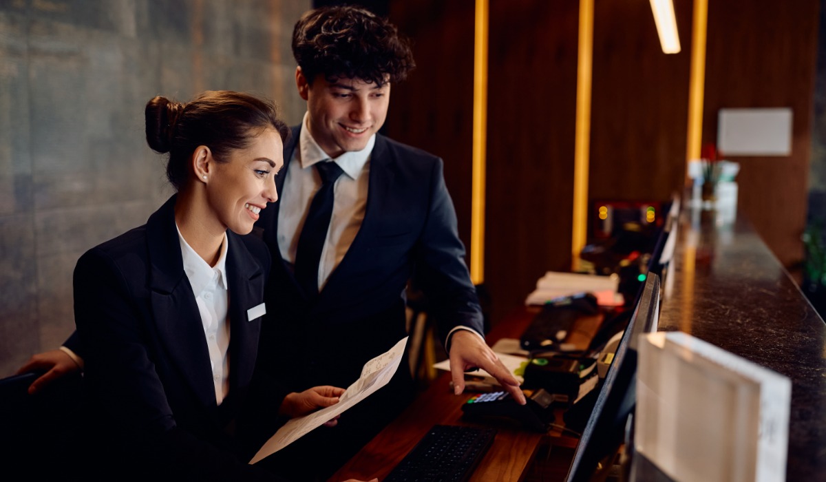 A smiling hotel reception team collaborating at the front desk.