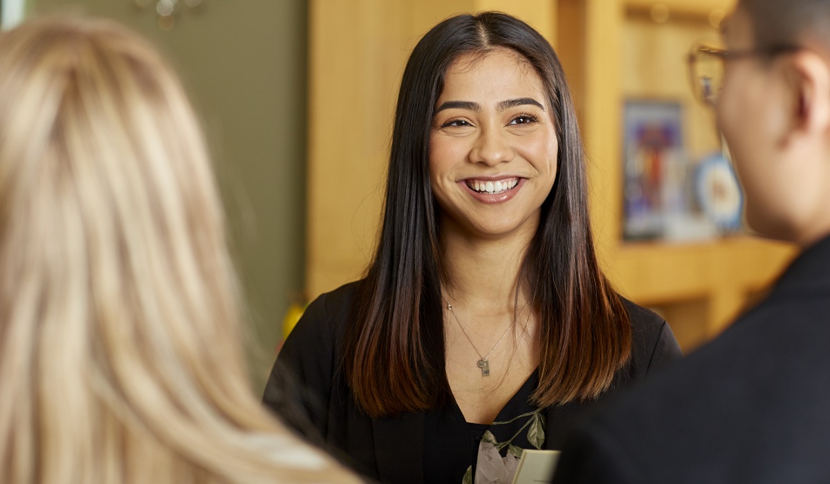 A smiling woman engaging in conversation with two people, showcasing a friendly and approachable atmosphere.